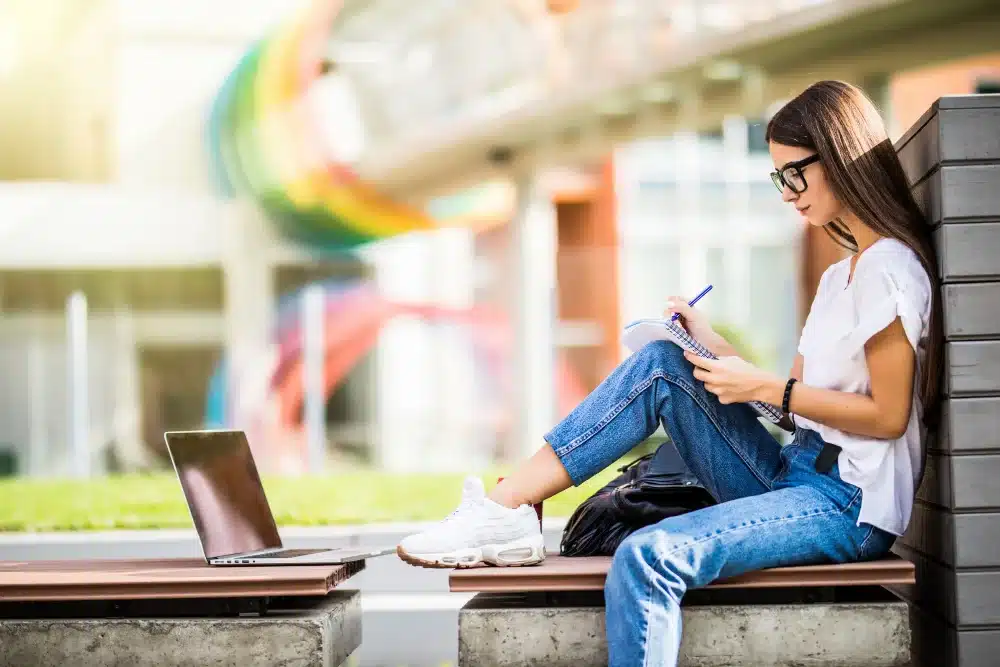 Mujer sentada con cuaderno y computador para estudiar ingles en el exterior