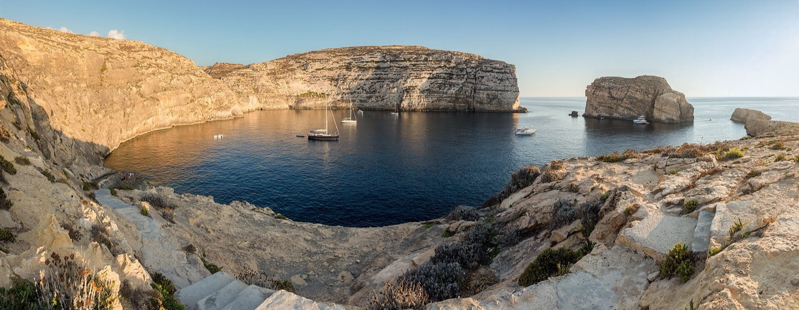 Bahía de Dwejra en la isla de Gozo, Malta, con acantilados de piedra caliza y veleros