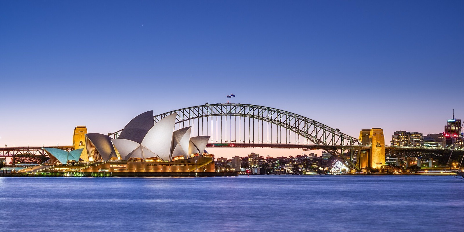 Ópera de Sídney y Harbour Bridge al anochecer, vistos desde el otro lado de la bahía